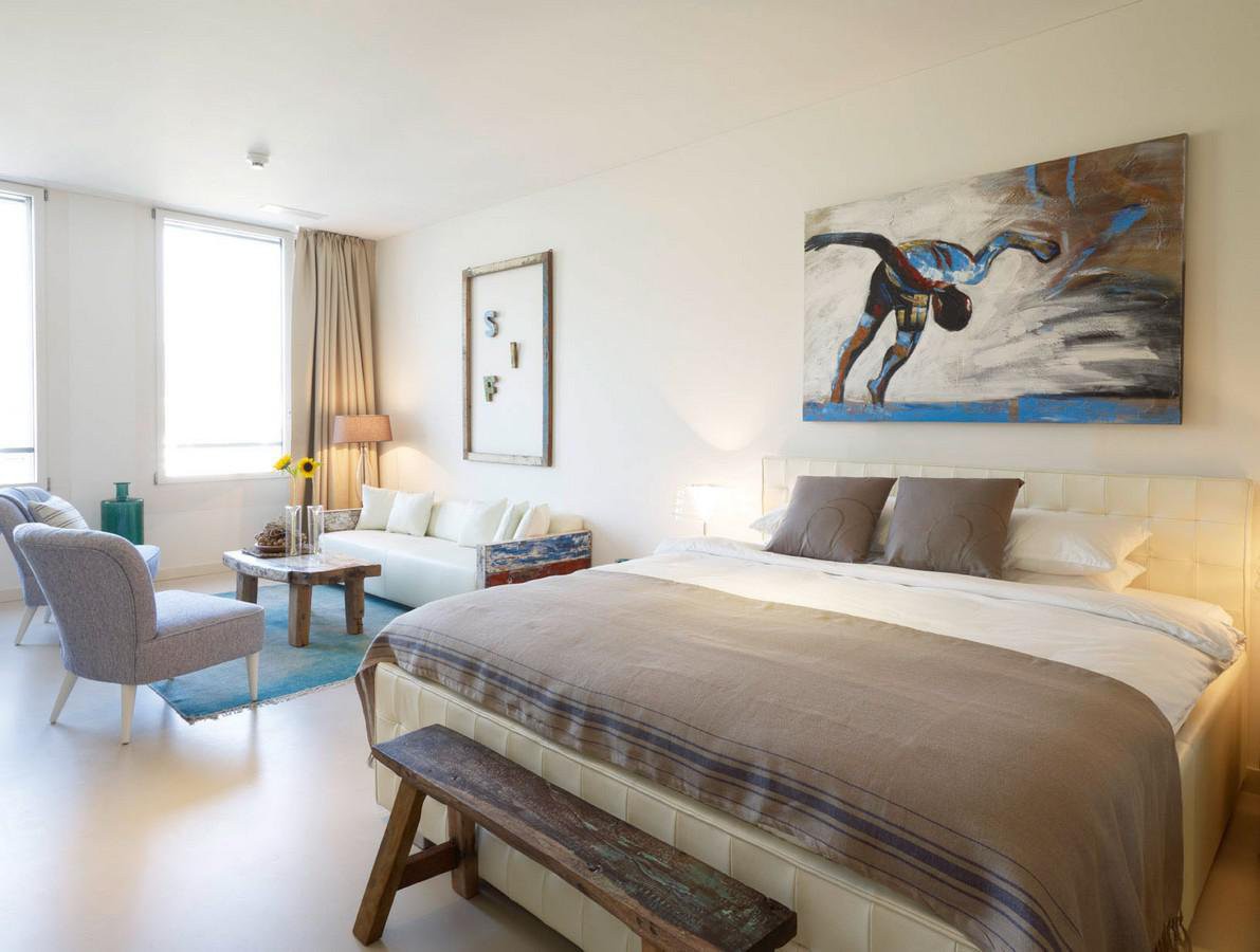 Modern bedroom with white walls, bed, wooden bench, lamp, painting, living room, sofa, coffee table, armchair, rug, window, sunflowers