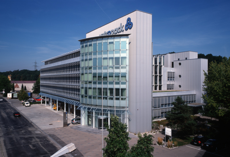 modern office building, glass facade, multiple floors, large parking lot, trees, cars parked