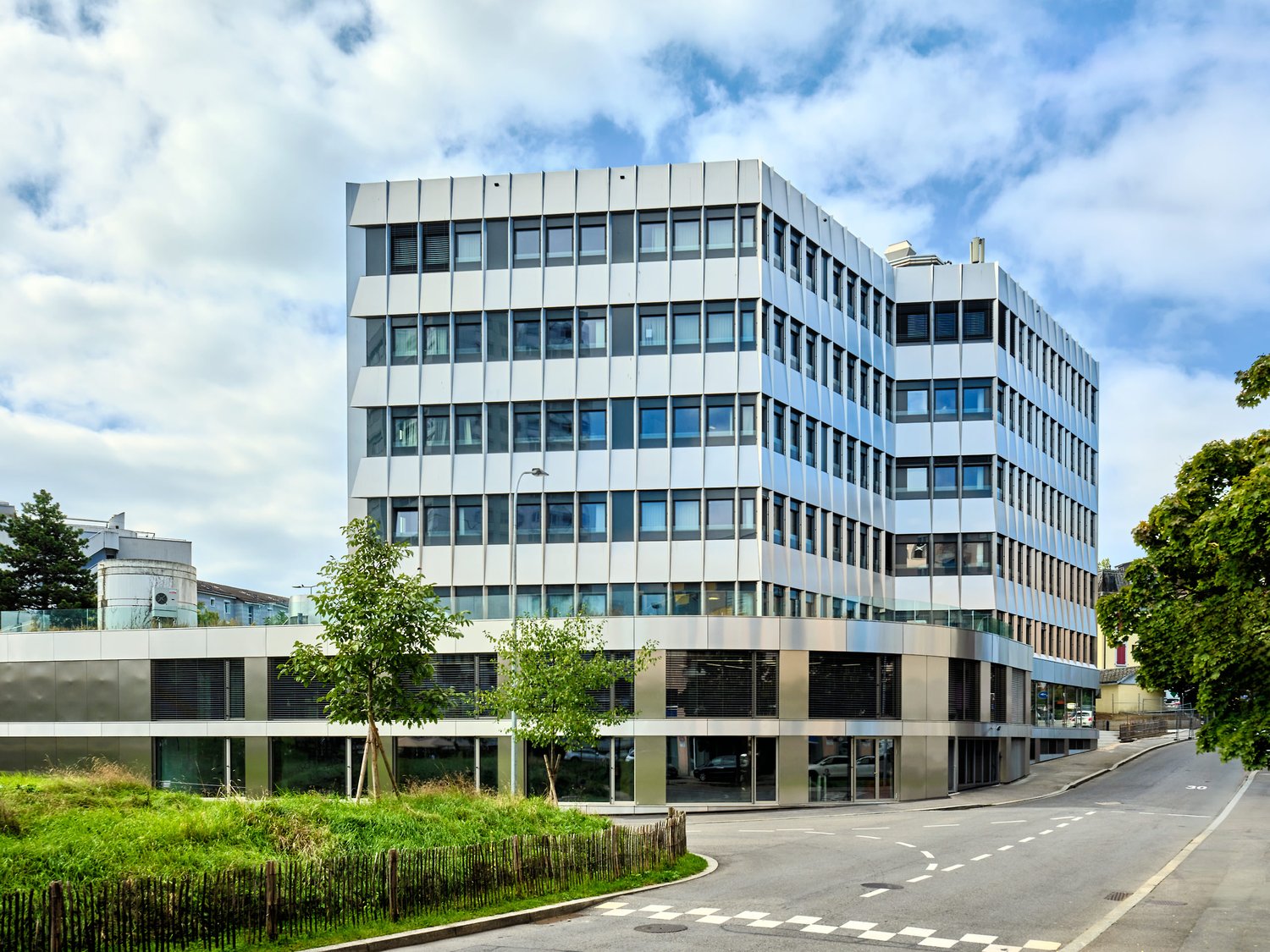 Modern office building, multiple floors, glass windows, metallic façade, greenery around