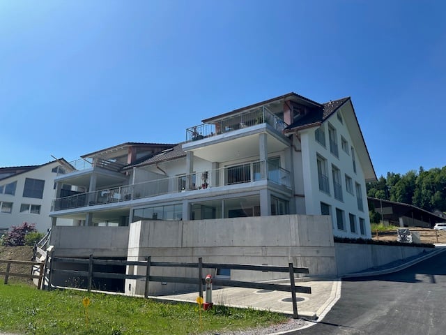 Multi-story apartment building with white exterior, balconies, and a sloped roof.