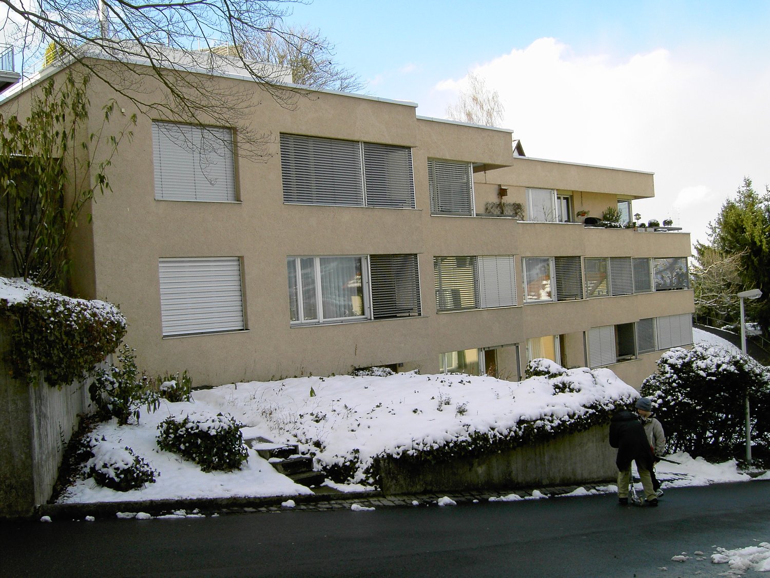 Apartment building with balcony, three floors, beige exterior, large windows, snowy surroundings
