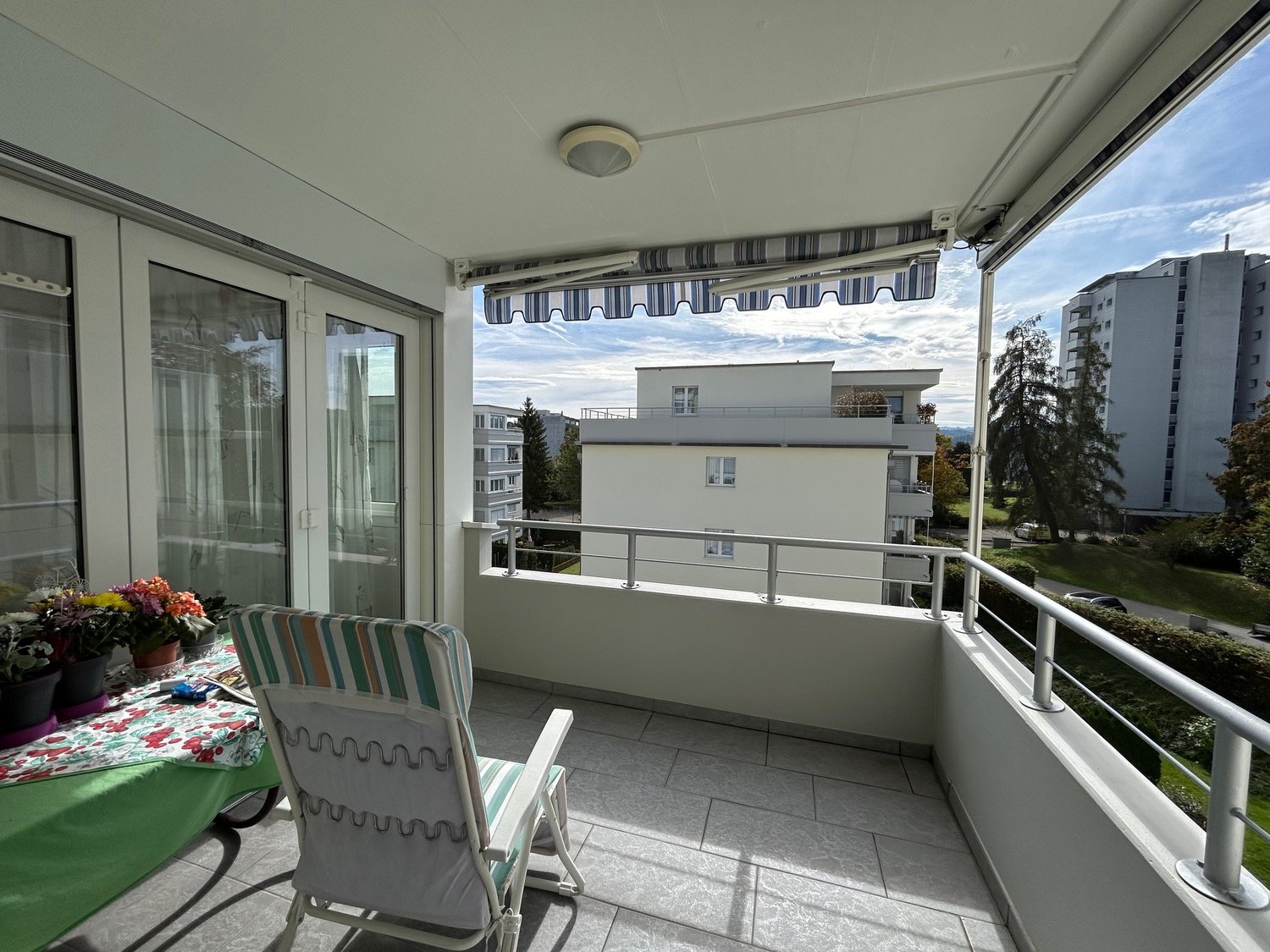 Balcony with patio furniture, sliding glass doors, view of surrounding buildings and greenery