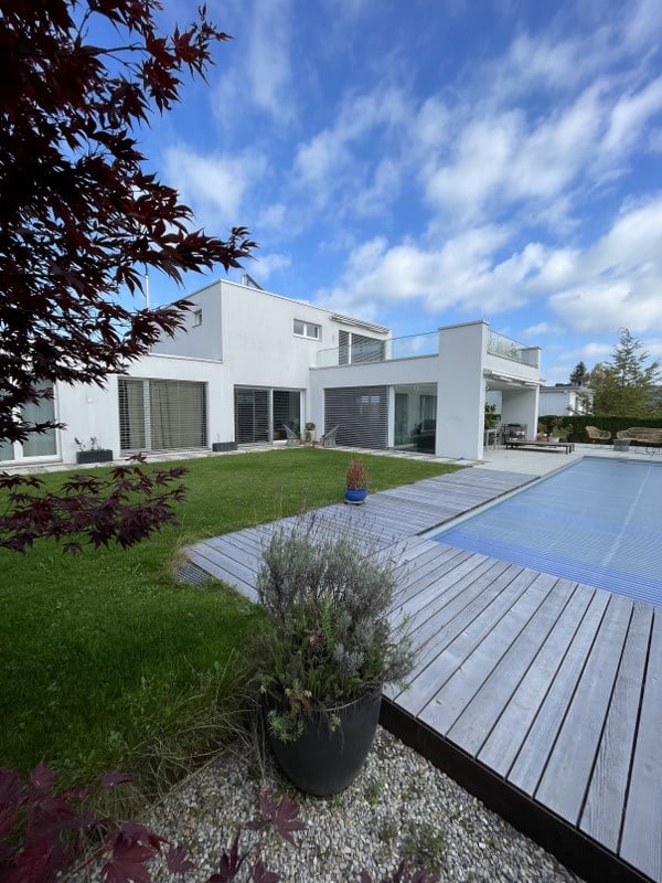 White villa, large garden, wooden deck, swimming pool, clear blue sky, lush green grass