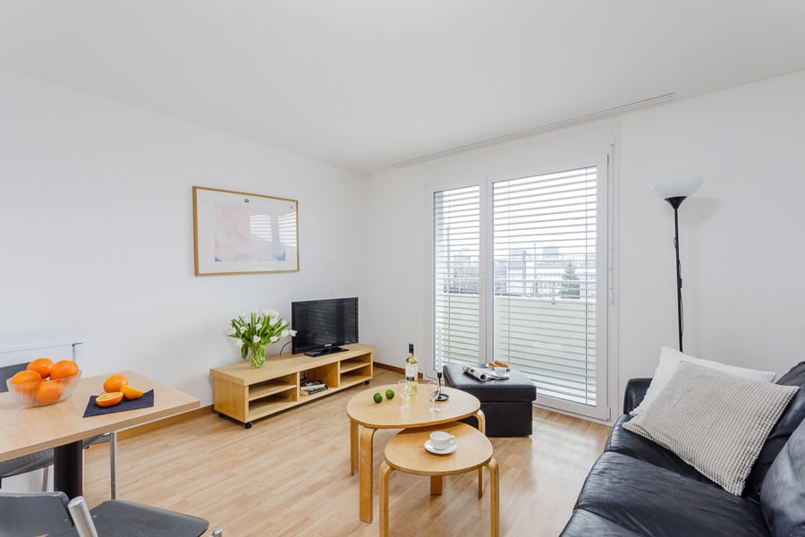 Bright and spacious living room with hardwood floors, white walls, large windows, TV stand, coffee table, and sofa