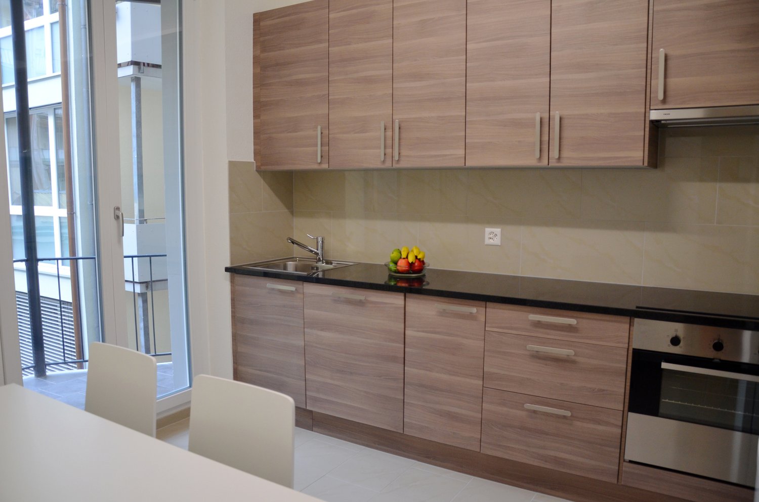 Modern kitchen with wooden cabinets, black countertop, stainless steel sink, and a dishwasher. Large windows provide natural light and a view of the exterior. The kitchen also includes a dining area with a table and chairs.