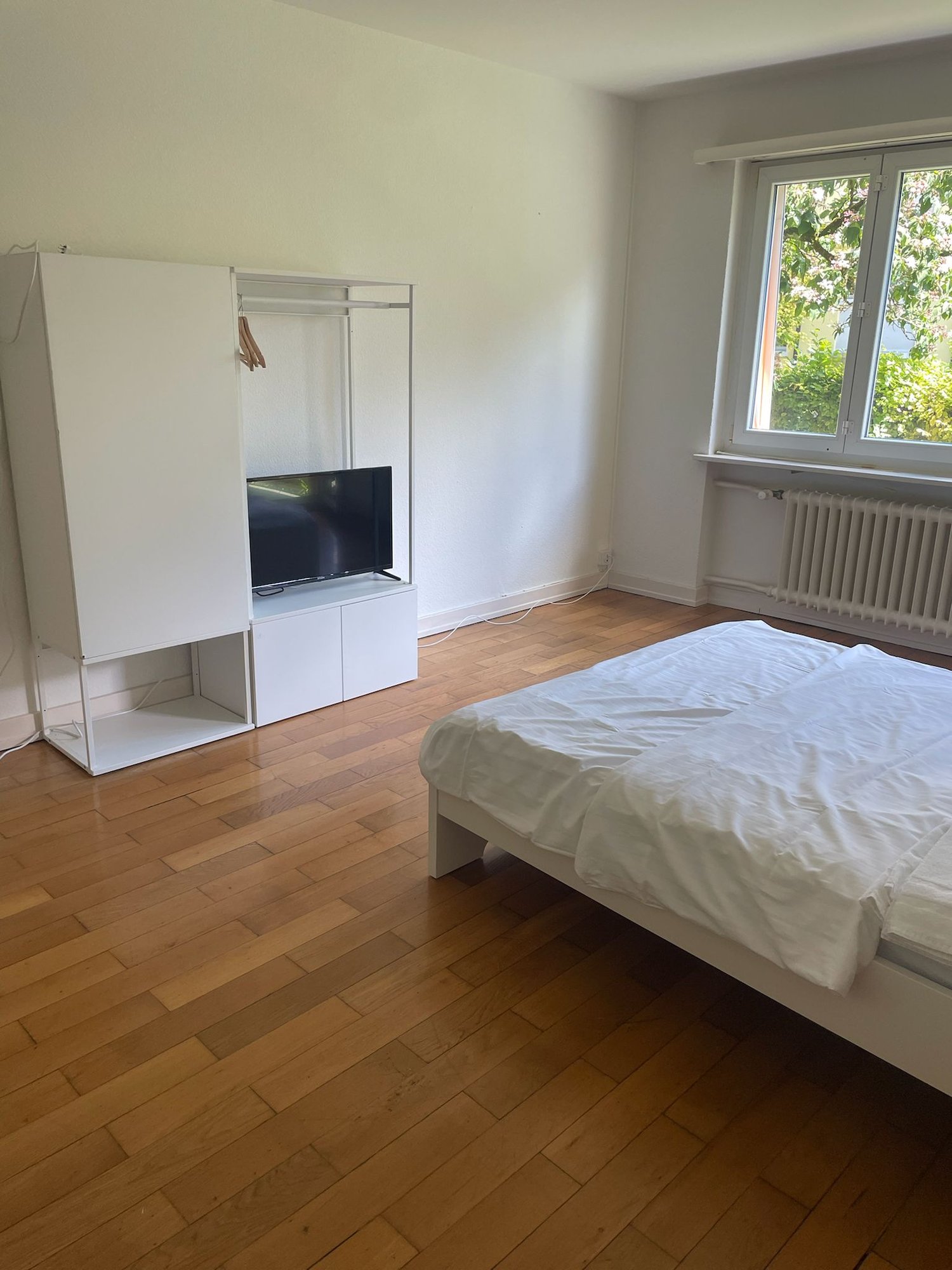 bed, white wardrobe, flat screen TV, wooden floor, window, radiator