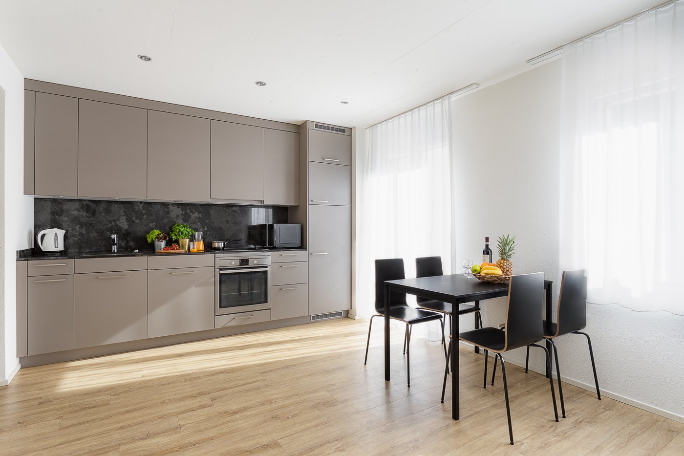 modern kitchen, wooden floor, kitchen island, gas stove, microwave, dishwasher, sink, grey cabinets, dining table with 4 chairs