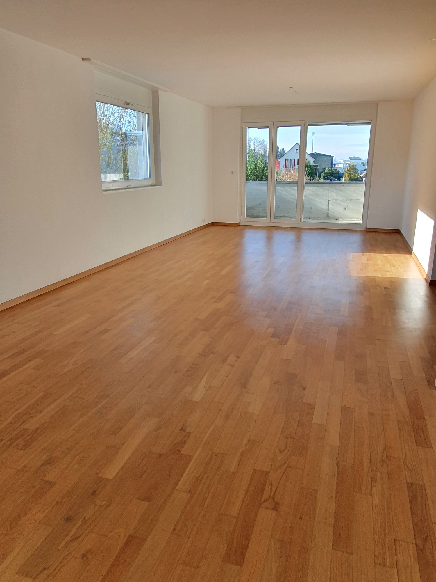 Empty room with wooden floors, white walls, glass sliding doors leading to a balcony, and a window.
