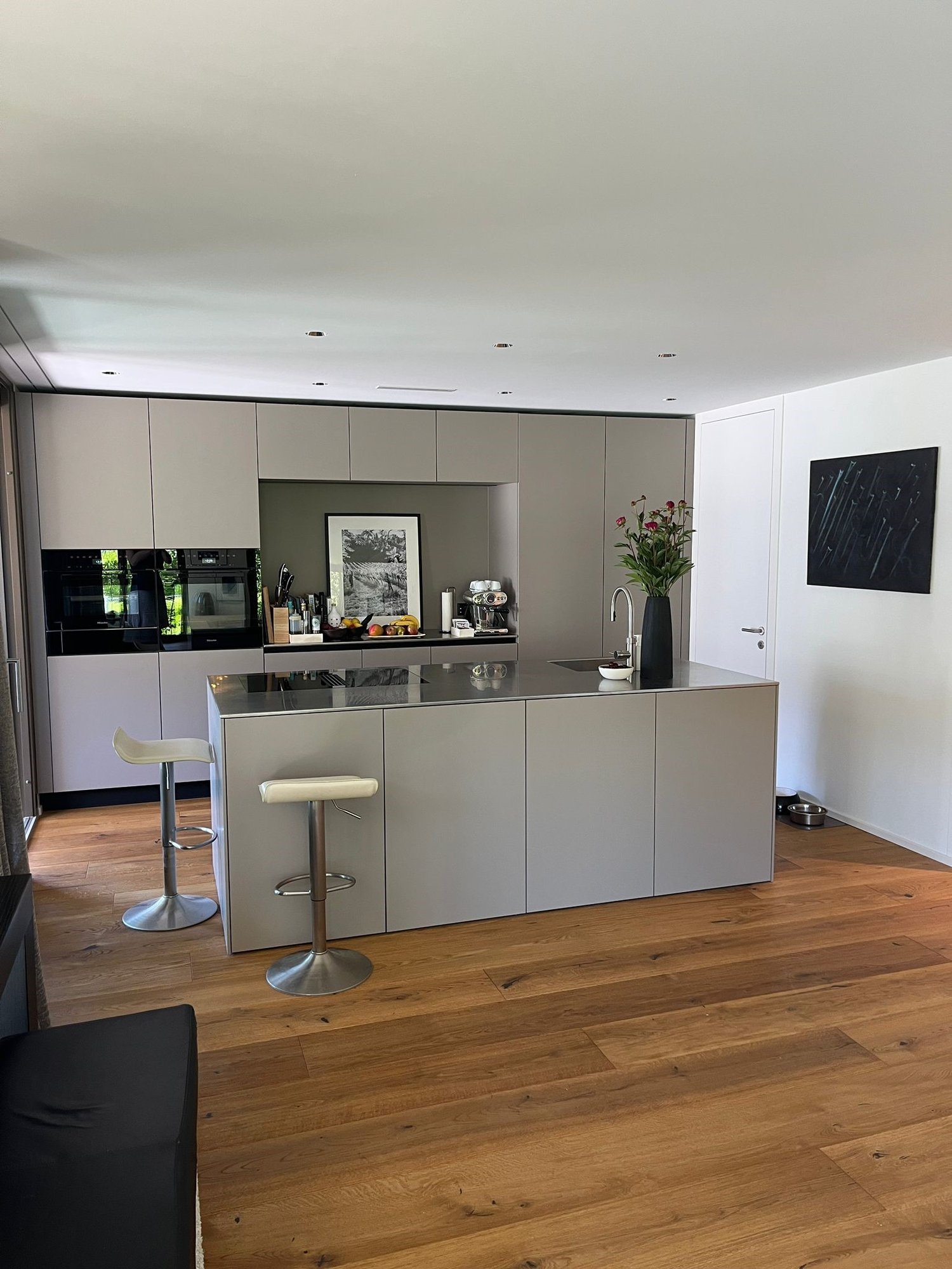 modern kitchen, island, gray cabinets, white countertops, central island with stove, sink, and faucet, two bar stools, flowers, picture frame, dog bowl