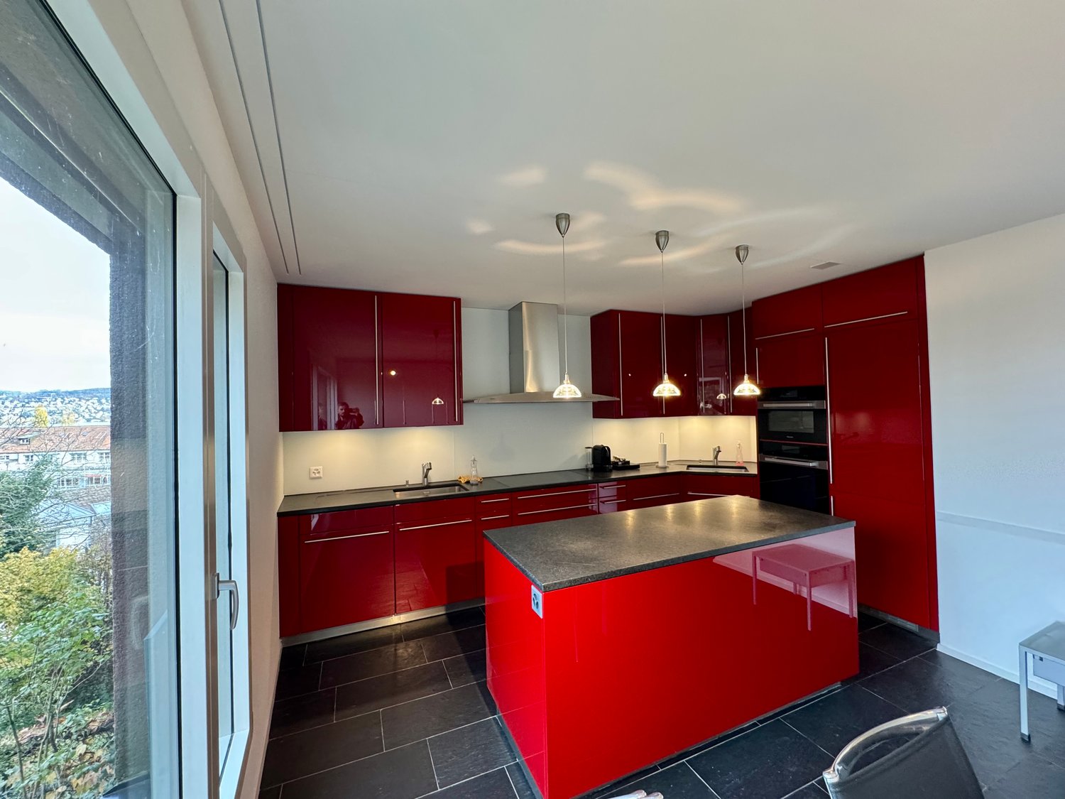 Modern kitchen with red cabinets, black countertops, large window with city view