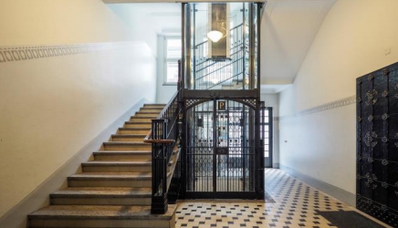 Wooden stairs with metal railing, tiled floor, high ceiling, large windows