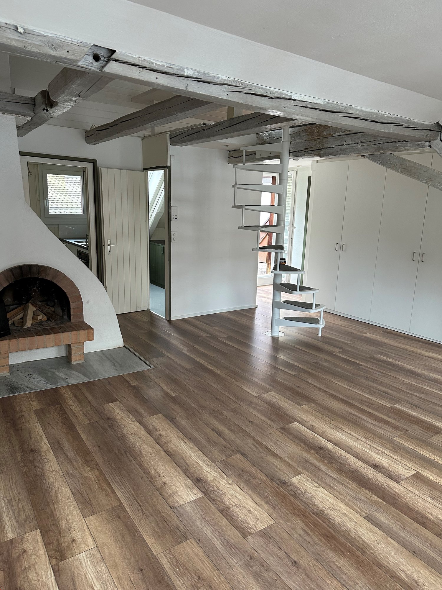 Open plan room, hardwood floors, spiral staircase, brick fireplace, large windows, closets, wooden beams, modern fixtures