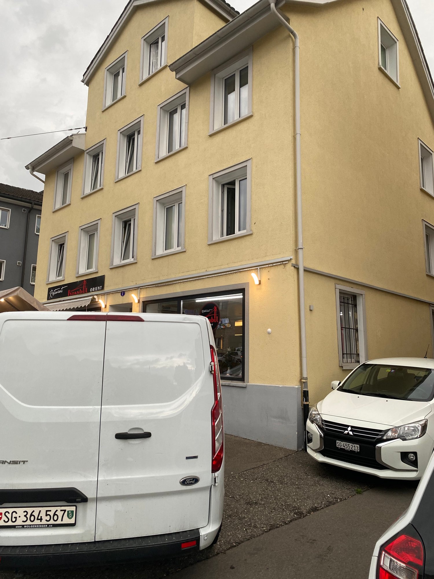 3 story building, yellow walls, large windows, cars parked in front, storefront on the ground floor