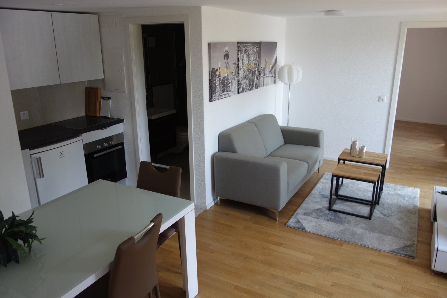 Open kitchen, dining table, couch, side tables, rug, artwork on wall