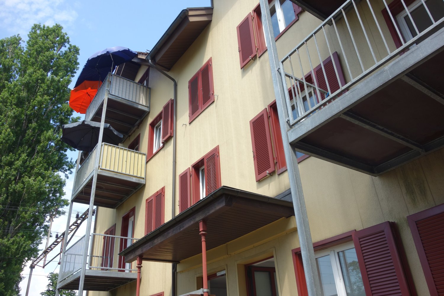 multi-story apartment building, yellow exterior, red shutters, multiple balconies