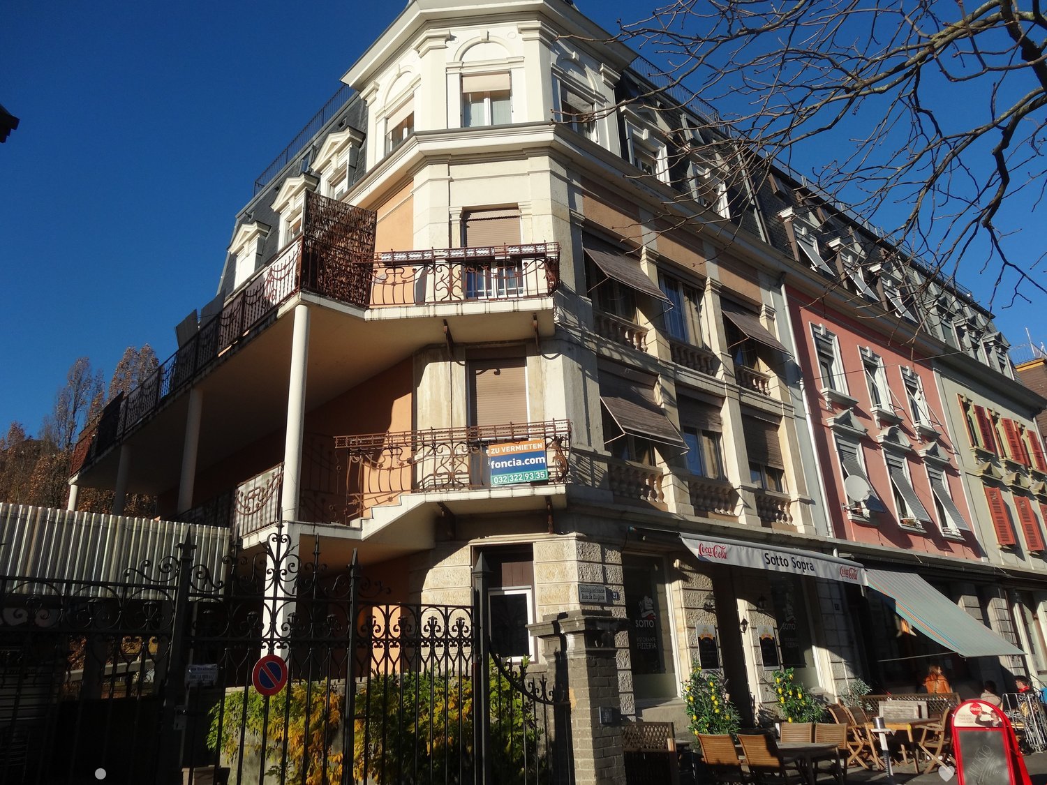 Multiple balconies, multi-story, black wrought-iron fencing, large arched windows, signage above the door