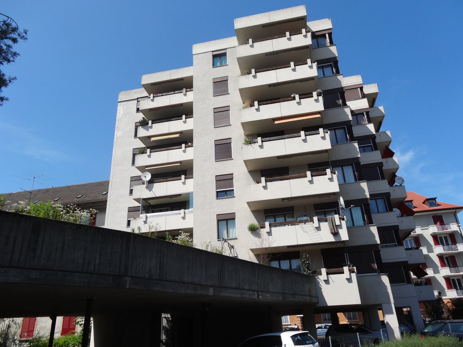 Multi-story building, balconies, concrete base, multiple parked cars