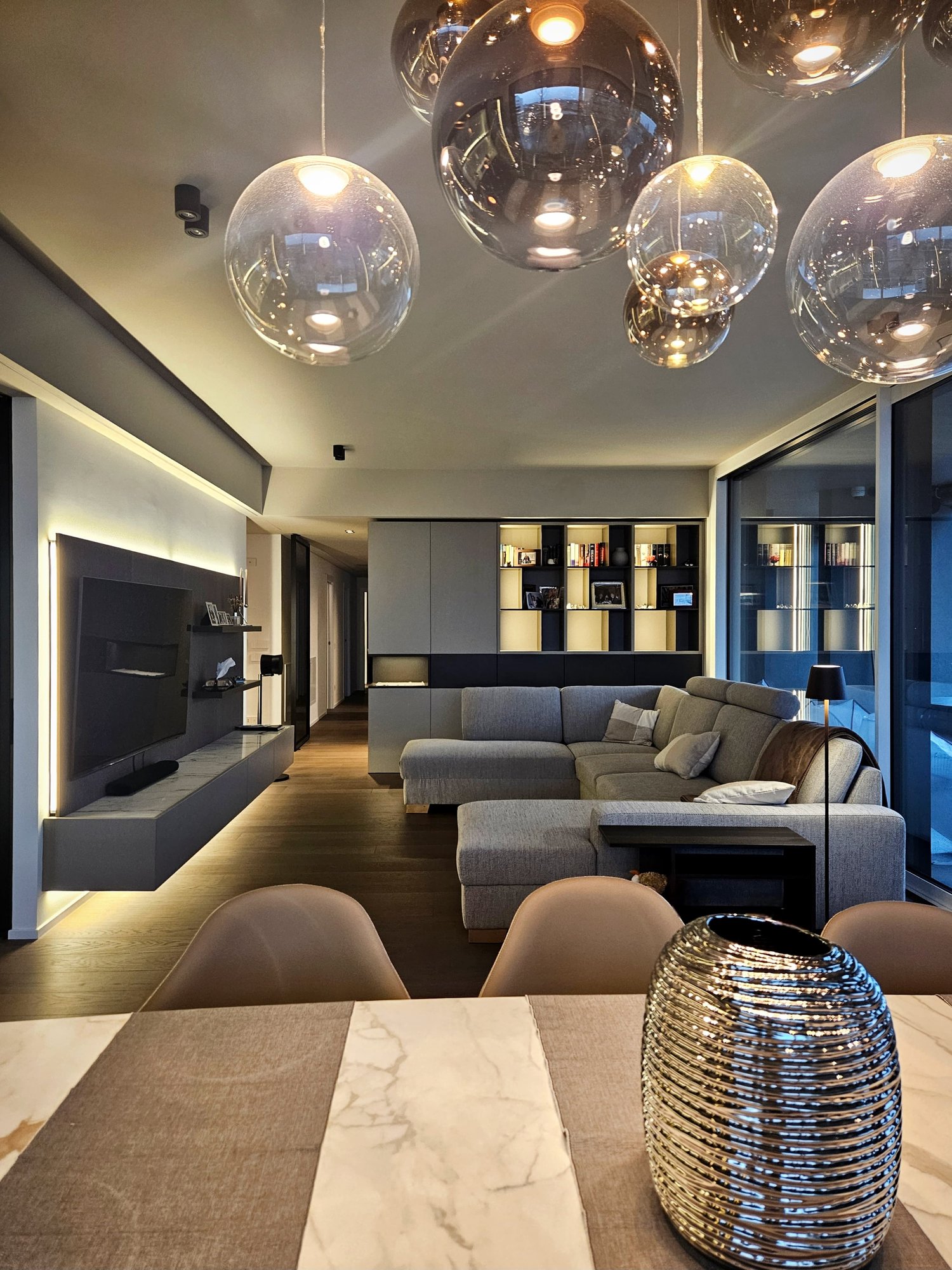 modern interior, gray sofa, wooden floor, TV mounted on wall, bookshelf, round table with vase, round hanging lamps