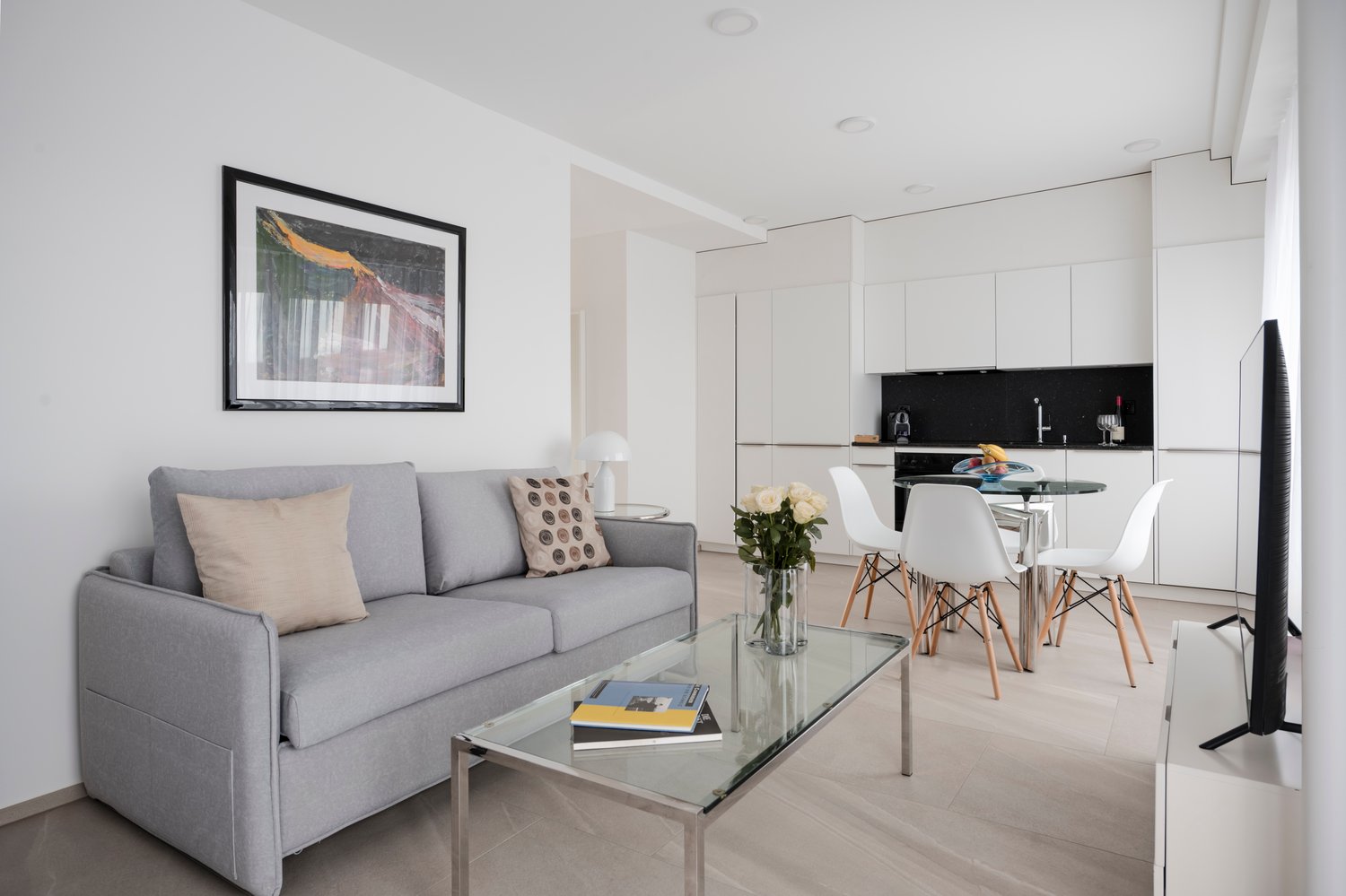 Gray couch, glass table, dining table and chairs, framed picture, white cabinets, and a TV