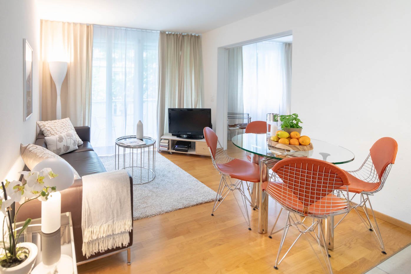 living room with couch, dining table, TV, floor lamp, plants, balcony with city view