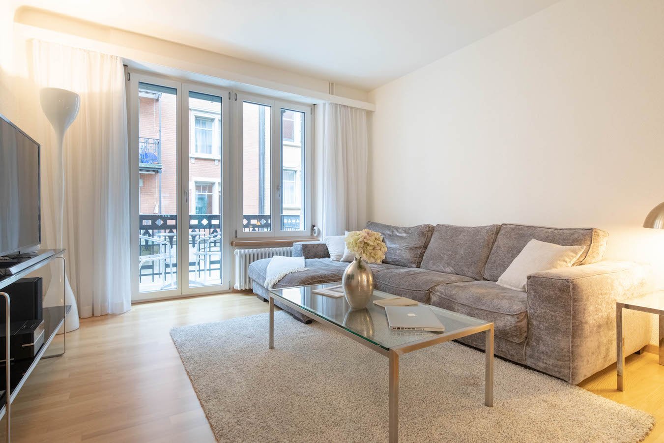 Living room with a couch, a coffee table, a carpet, sliding glass doors to the balcony, a television, and a lamp