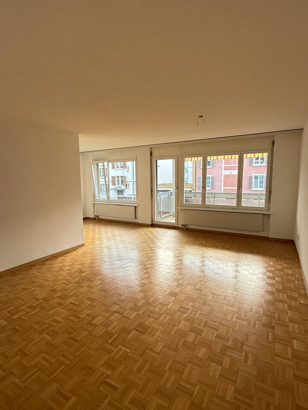 Large living room, wooden parquet flooring, high ceilings, large windows, city view