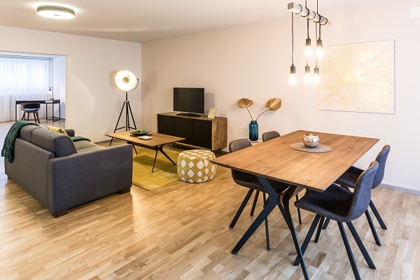 Open-concept living and dining area with hardwood floors, gray sofa, wooden dining table and chairs, TV stand, and decorative wall art