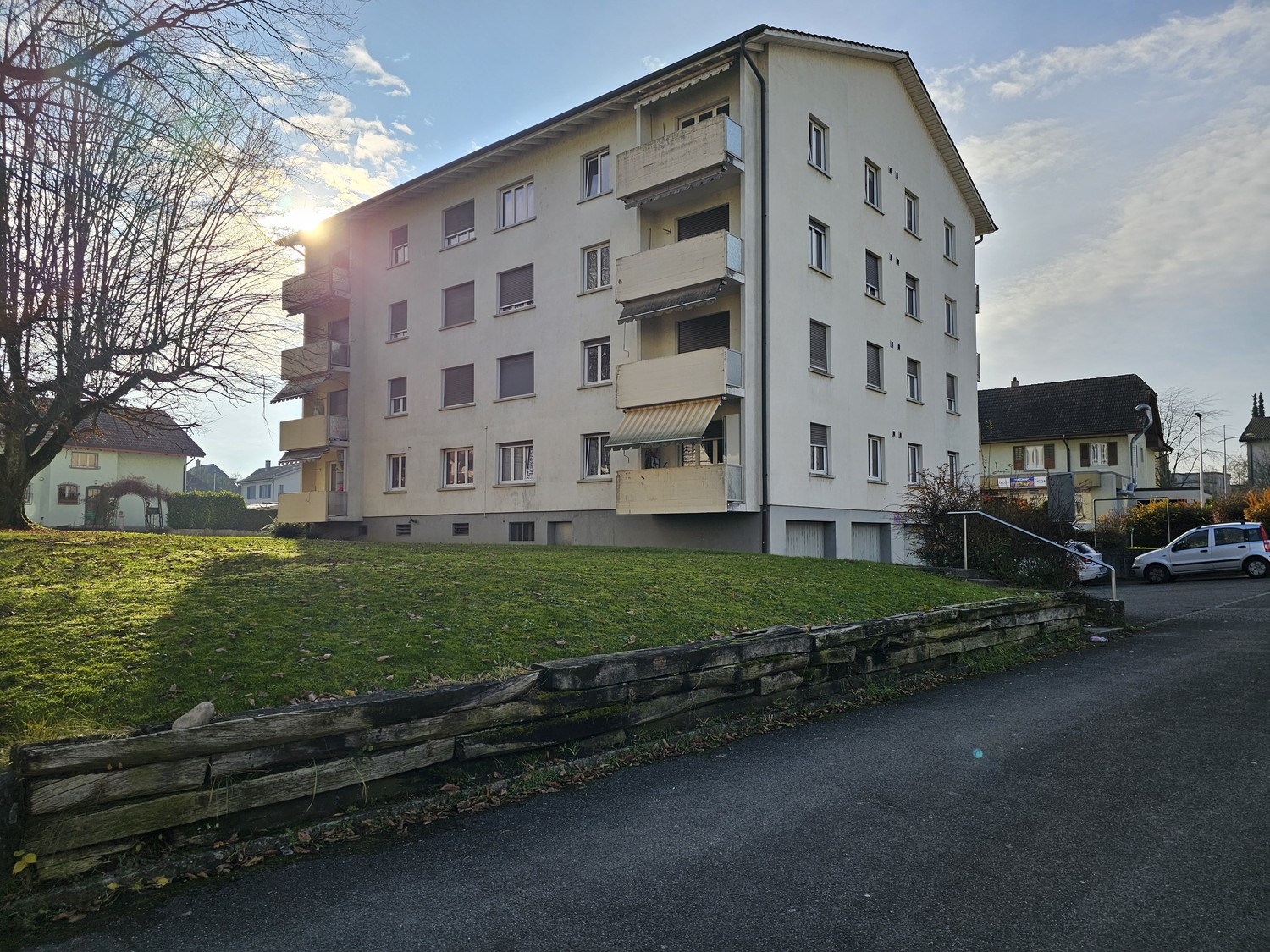 4-story apartment building with balconies, surrounded by a grassy area and a paved driveway