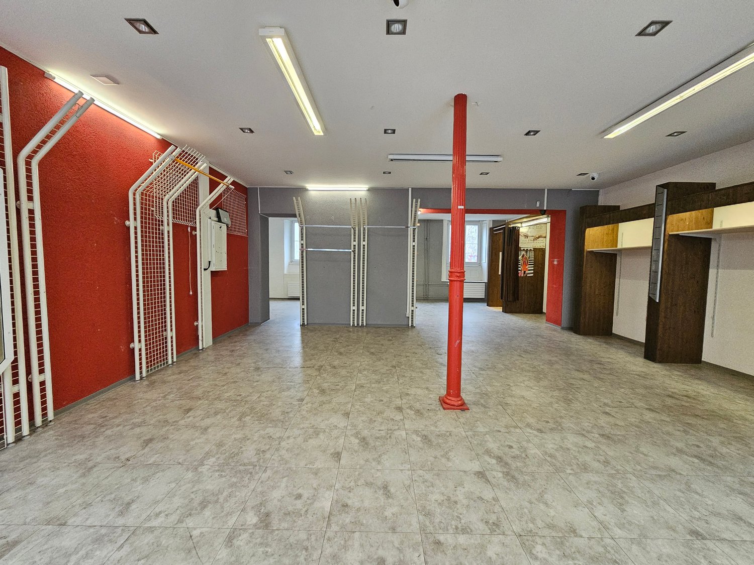 empty room, gray floor, red walls, red pillar, fluorescent ceiling lights, two doors, metal racks on the wall