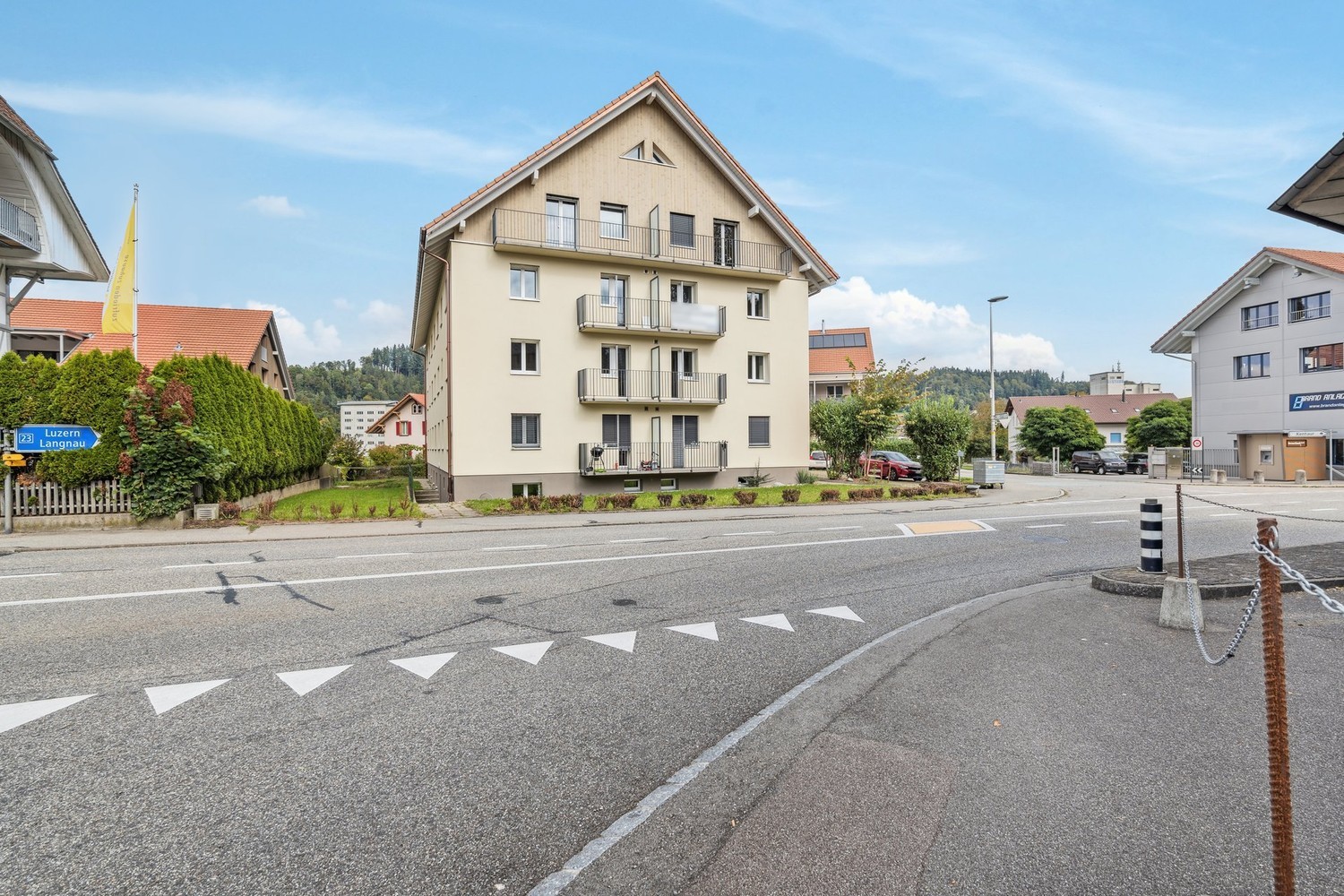 4-story apartment building with beige exterior, balconies, and a road in the foreground with road markings and a street sign.