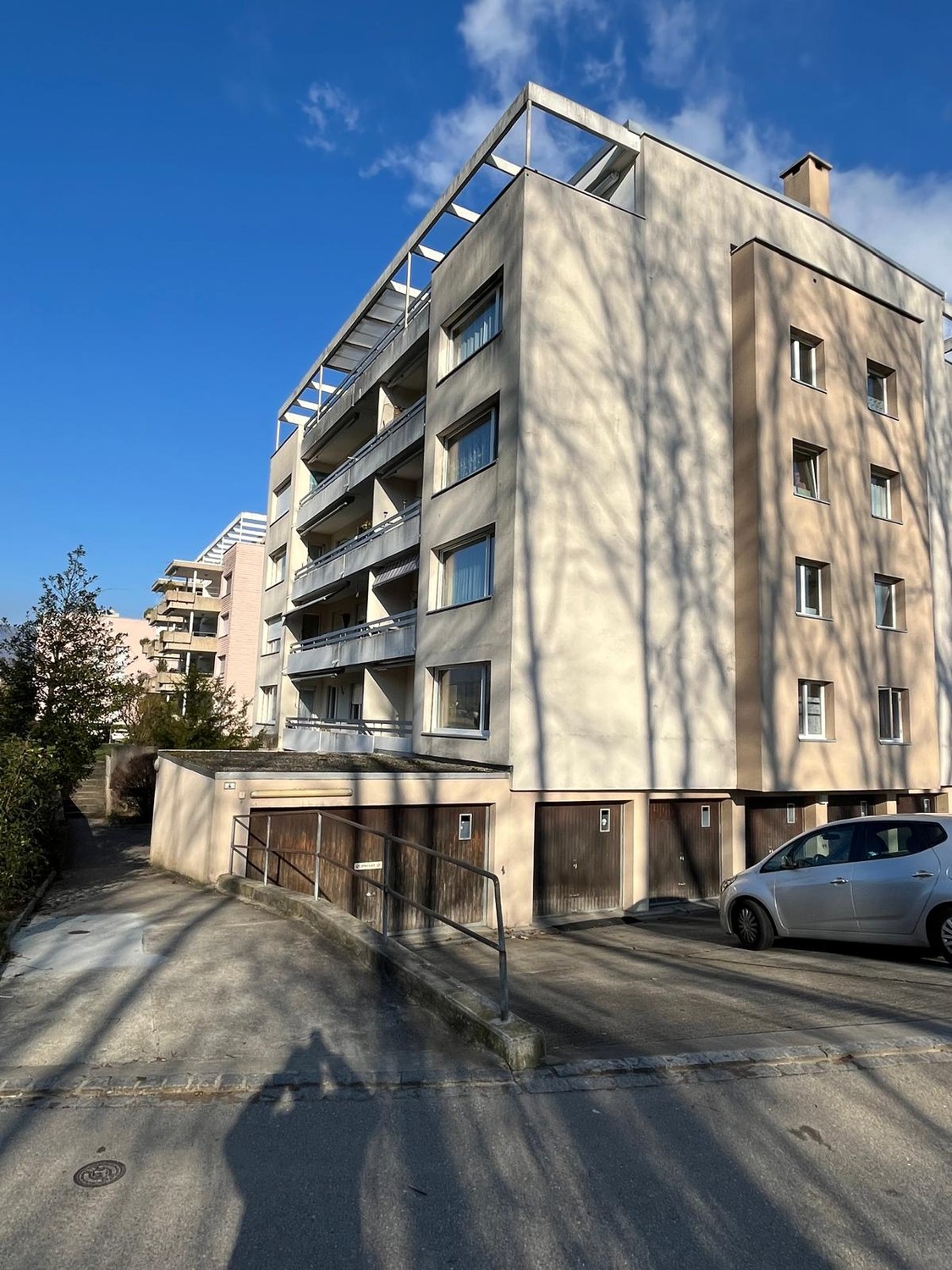 Multi-story apartment building with beige exterior, balconies, and a parking area in front