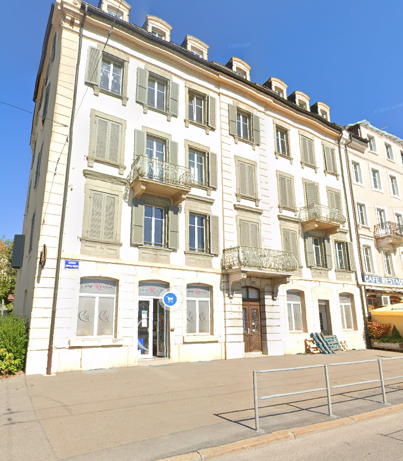 A multi-story building with a classical architectural style, featuring ornate facades, balconies, and large windows. The building appears to house a cafe or restaurant on the ground floor.