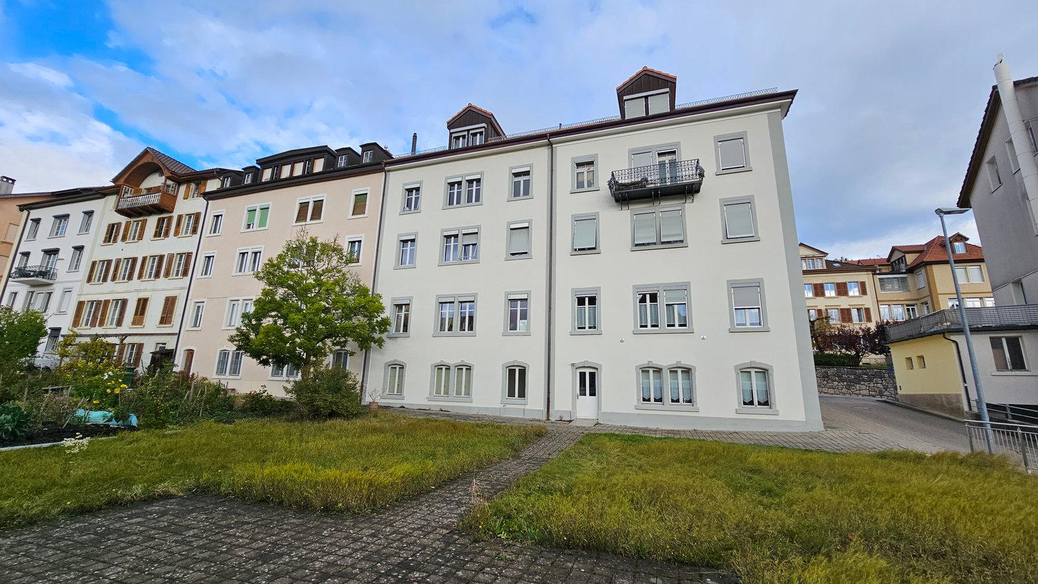 Multi-story apartment building with gray exterior, balconies, and a grassy area in the foreground