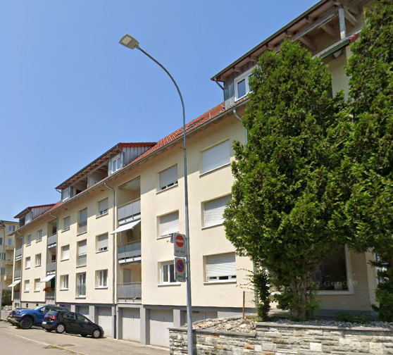 Multi-story apartment building with balconies, surrounded by trees and greenery