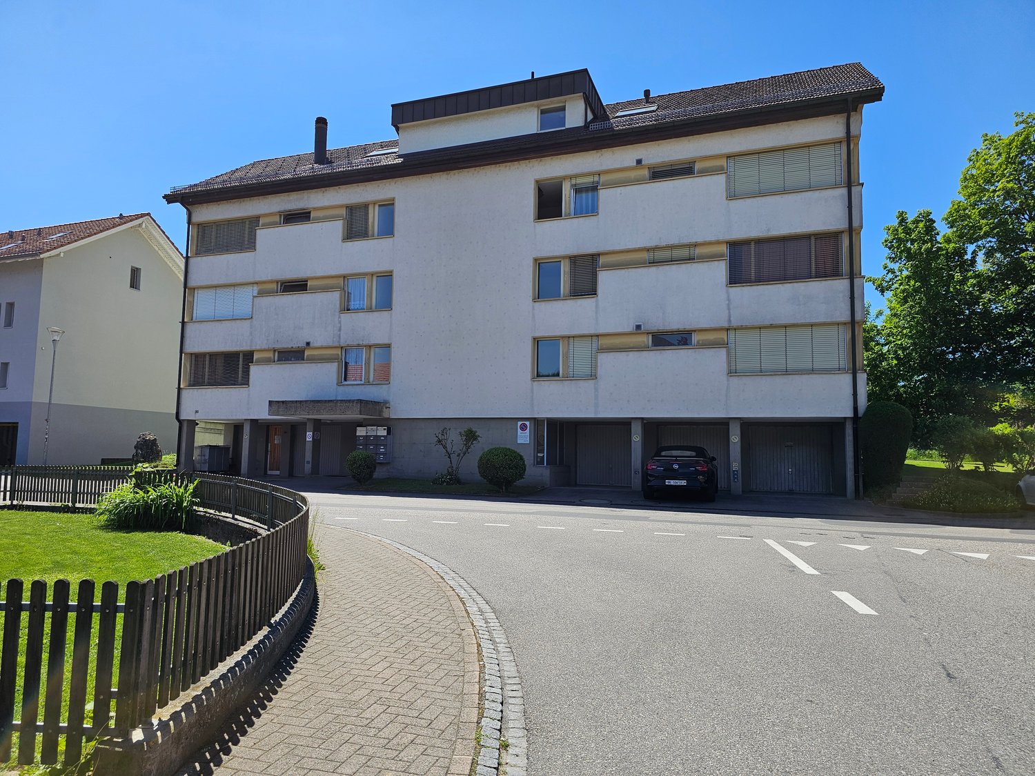 5 story building, white exterior, underground garage with two parking places, car parked, small lawn, shrubs, street light