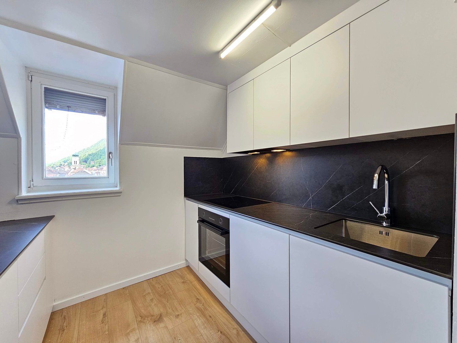 modern kitchen, white cabinets, black countertops, stainless steel sink, built-in oven, dishwasher, washing machine, window