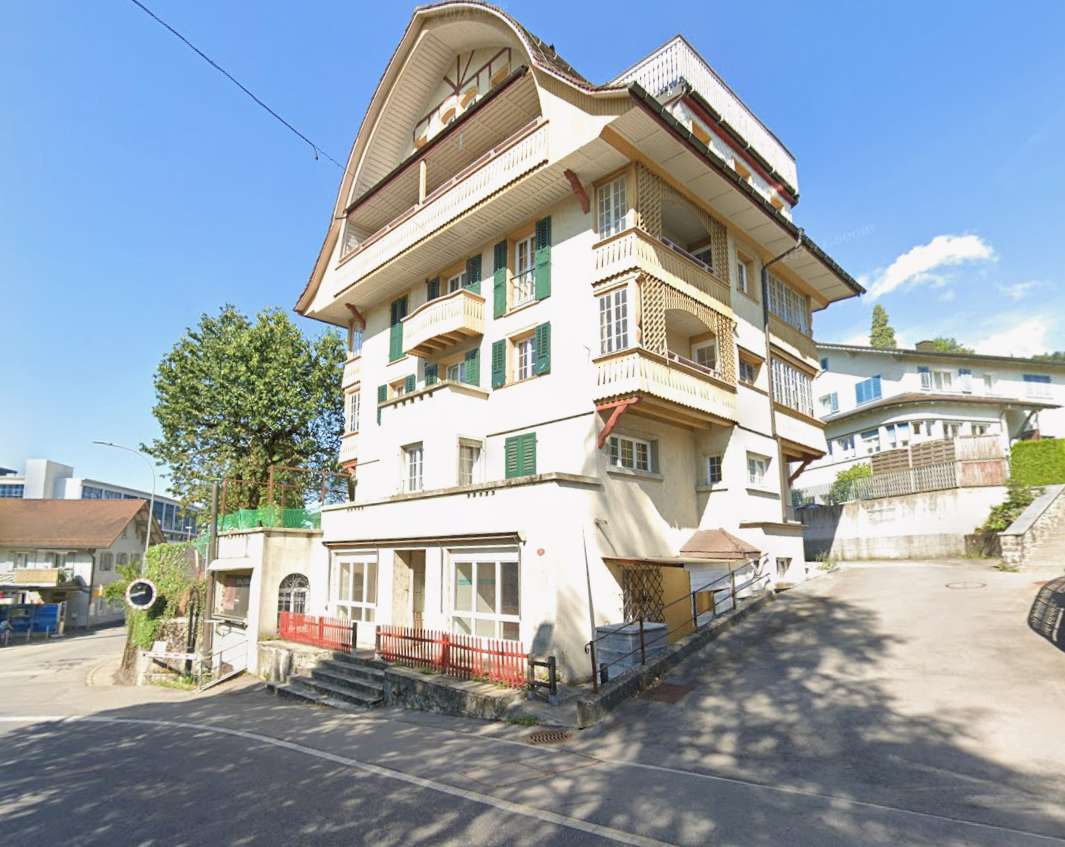 White building, multiple balconies, red railings, street entrance, multiple windows, two storeys