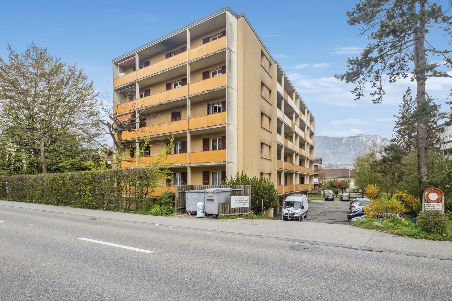 multistory building with balconies, trees and plants around, street view