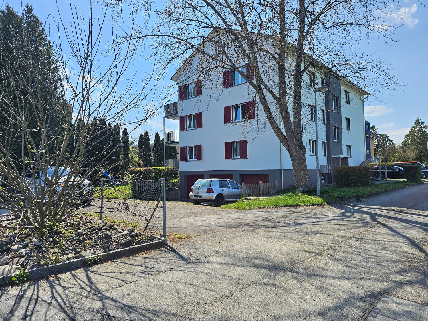 3 story white building, red shutters, garage, cars parked in front, tree, fence
