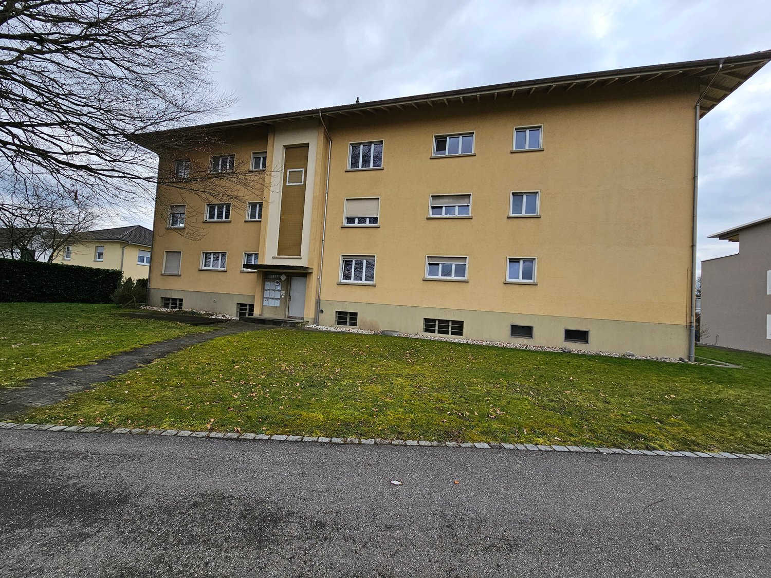 multi-story building, yellow exterior, several windows, walkway, well-maintained grassy area, sidewalk, paved driveway