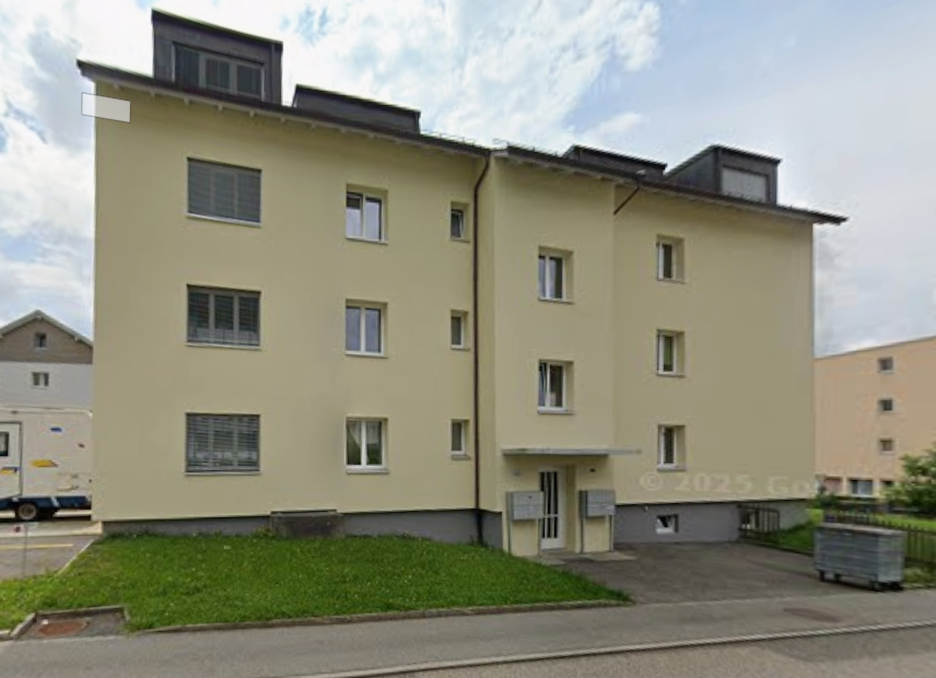 3 story building, raised ground floor, yellow facade, glass windows, garage, driveway, green lawn