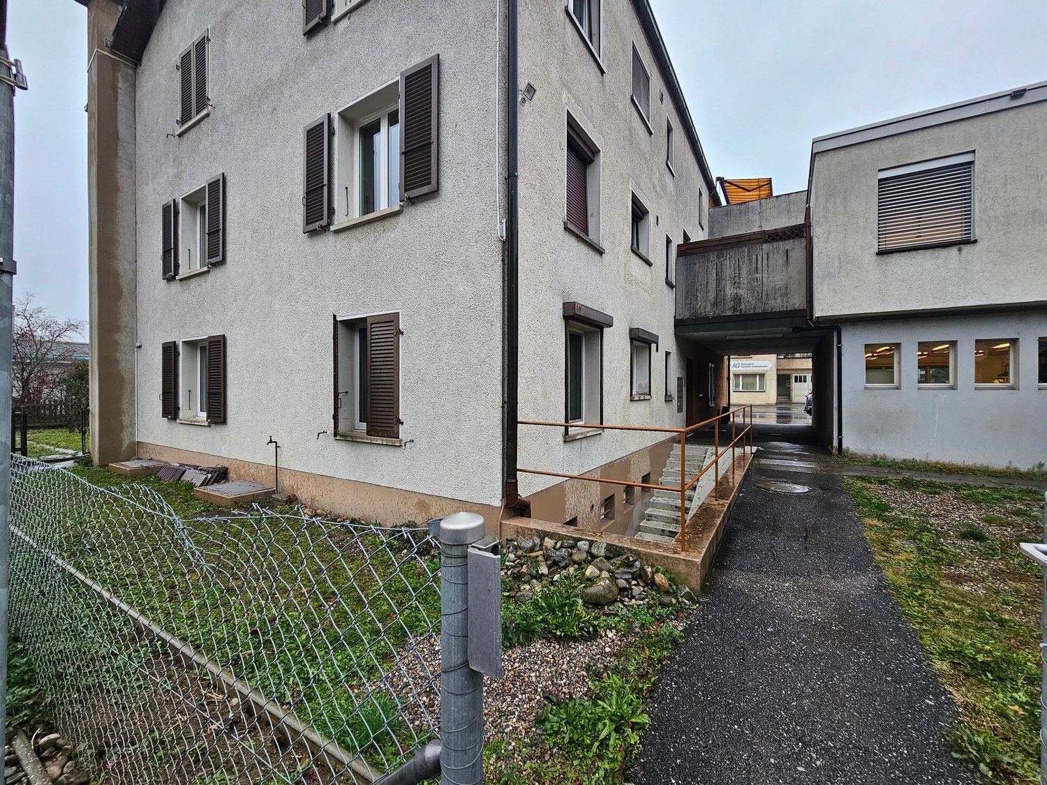 Gray building with multiple windows, concrete wall, and small stairs