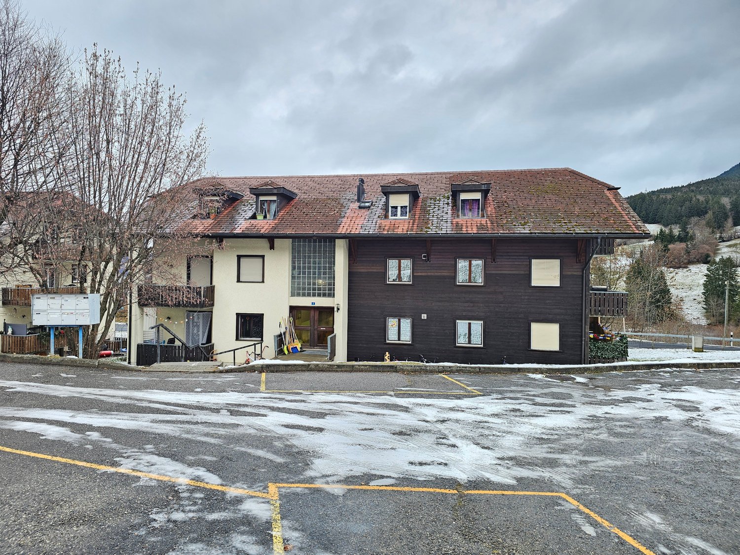 2 story building with brown roof, wooden facade, several windows, entrance with door, parking space
