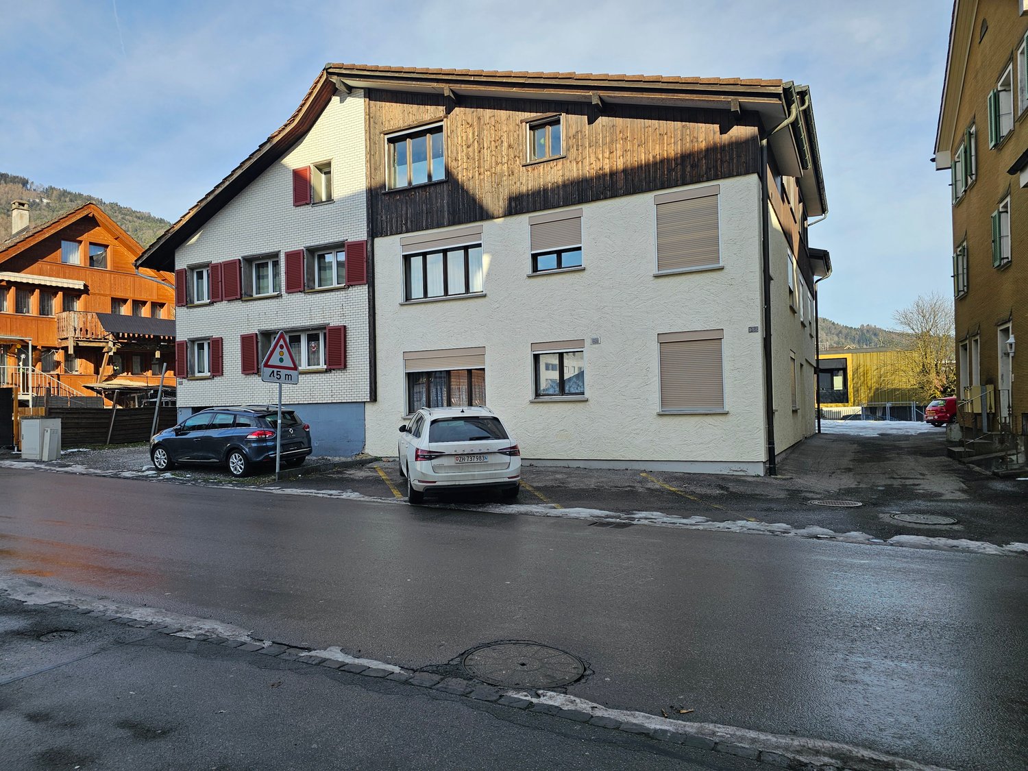3 story house, white walls, brown roof, red shutters, cars parked