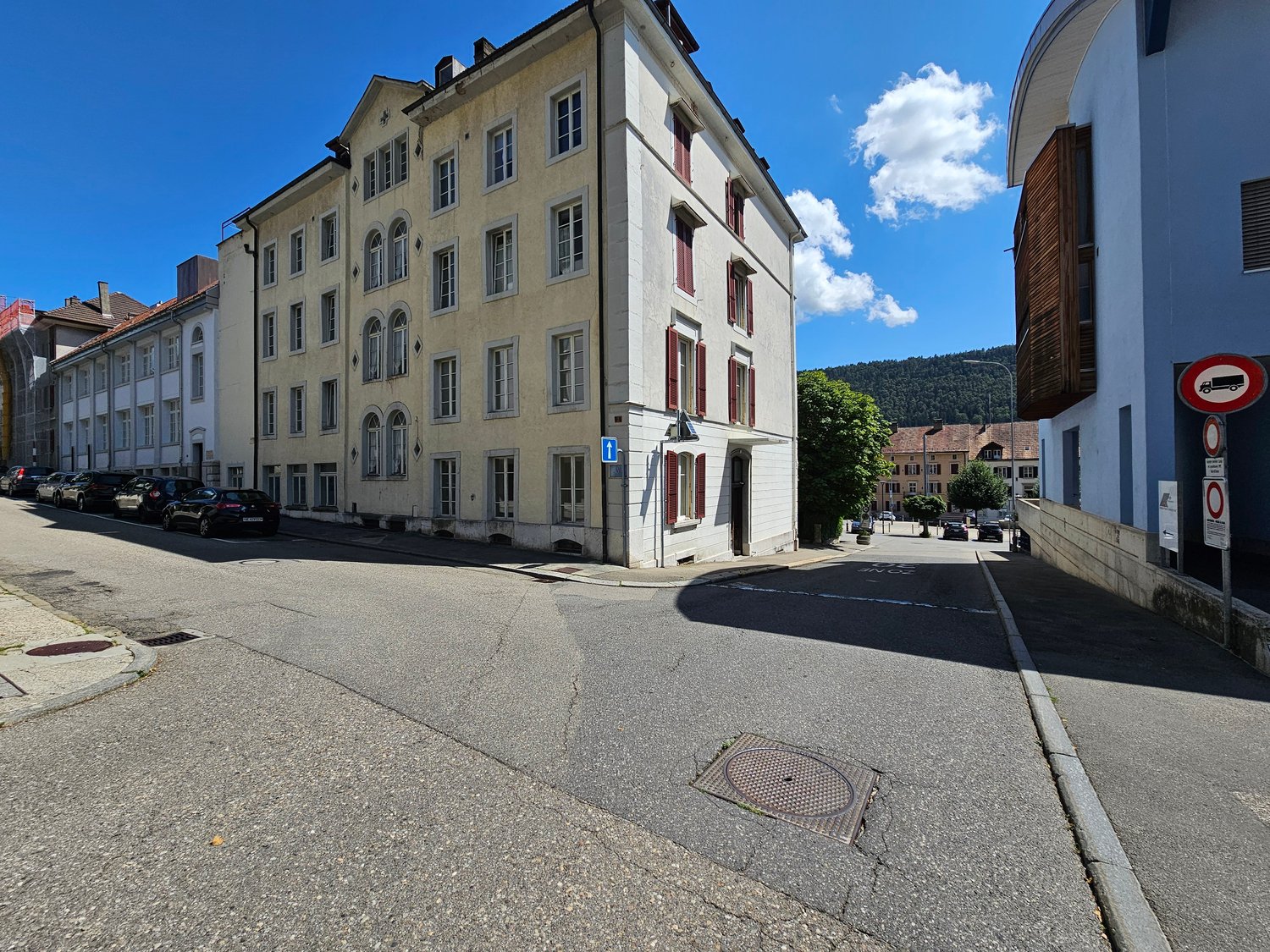4 story building, yellow exterior, red window shutters, blue handicap parking sign, corner street, cars parked on the street