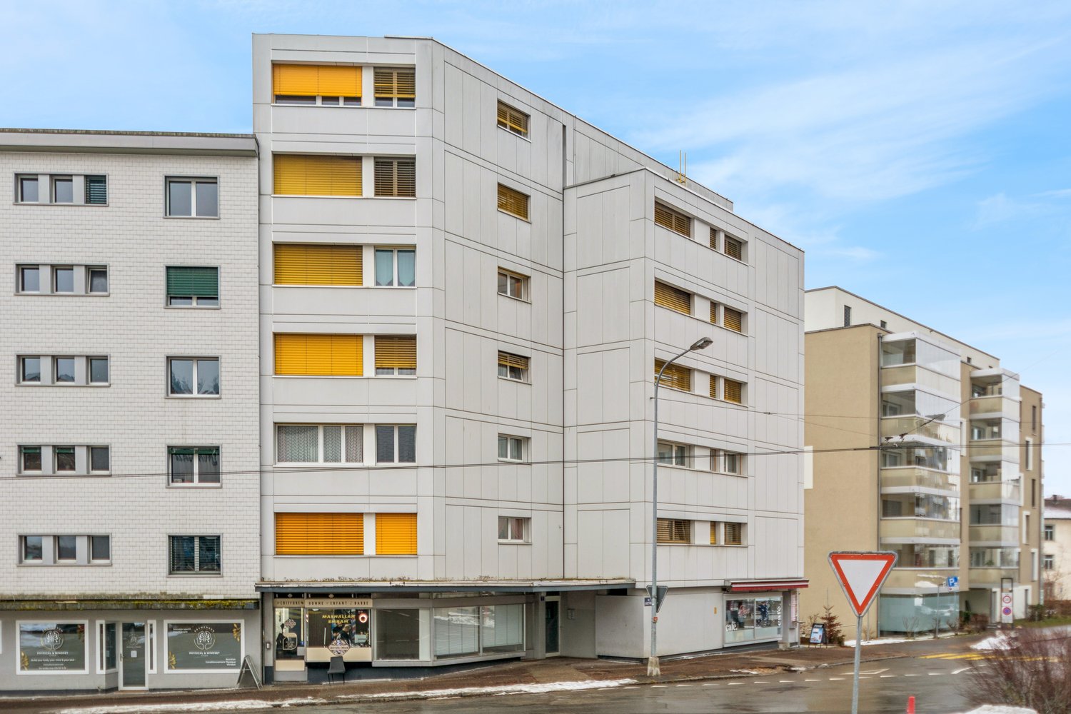 modern white high-rise building, yellow shutters, commercial spaces on the ground floor, street light