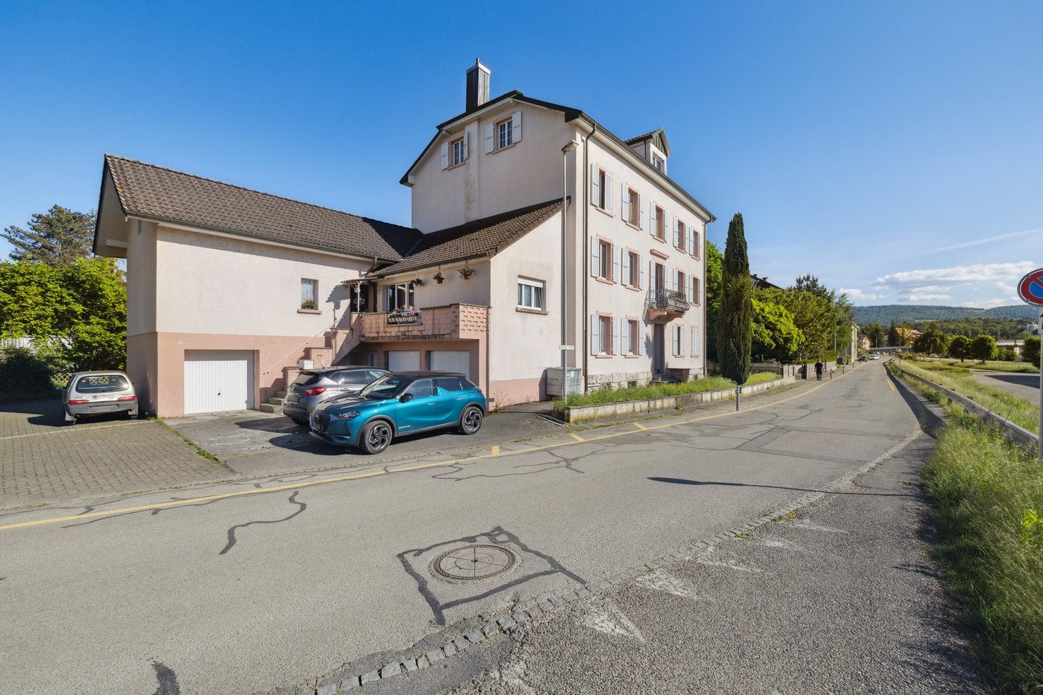 2-story house, tan and pink exterior, brown roof, large windows, 2 cars parked in garage, driveway