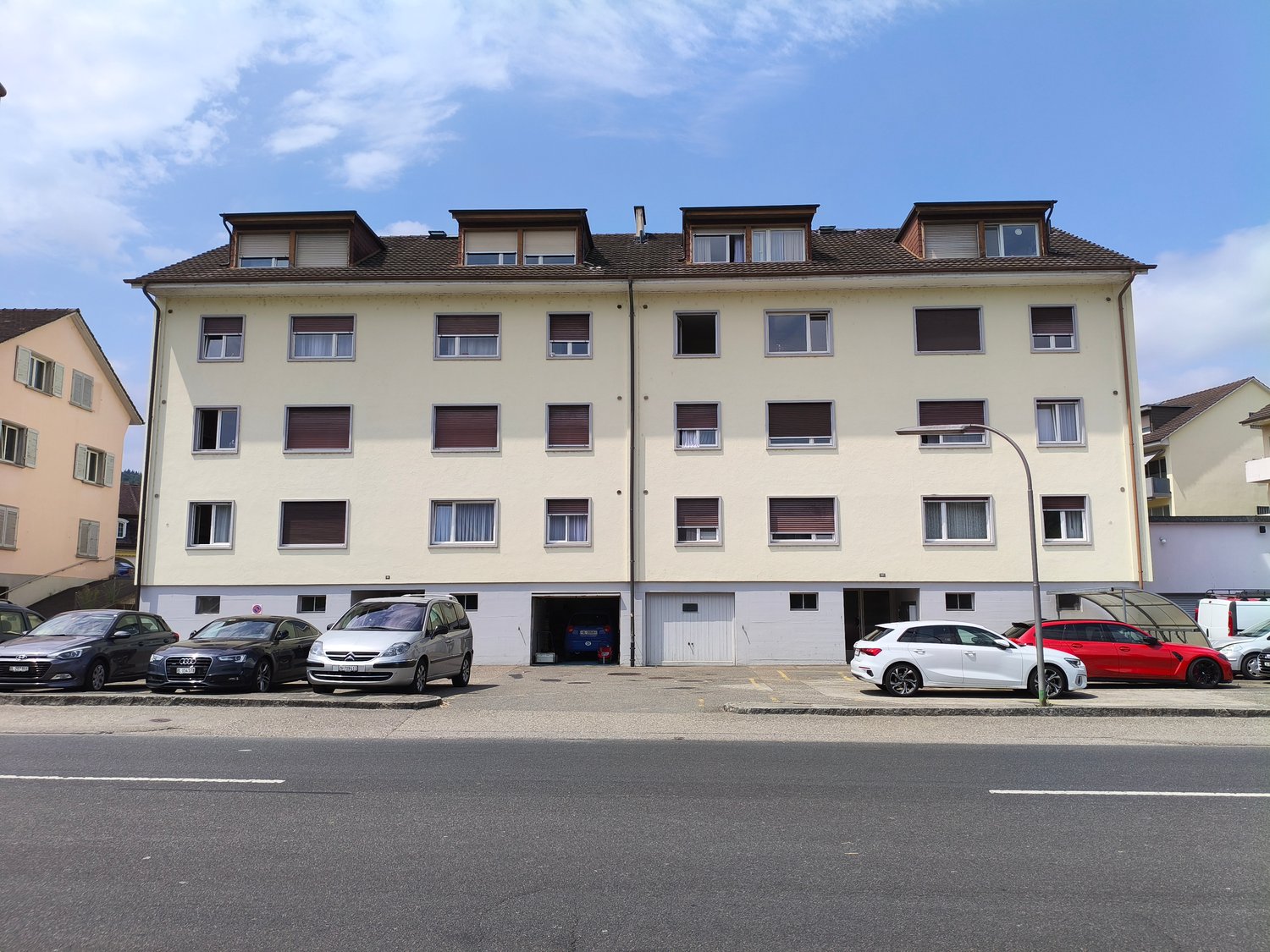4 story apartment building, beige exterior, multiple windows, garage, multiple cars parked in front