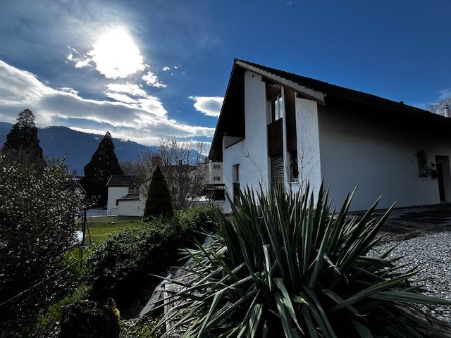 white facade, black roof, windows, garden, mountain in background