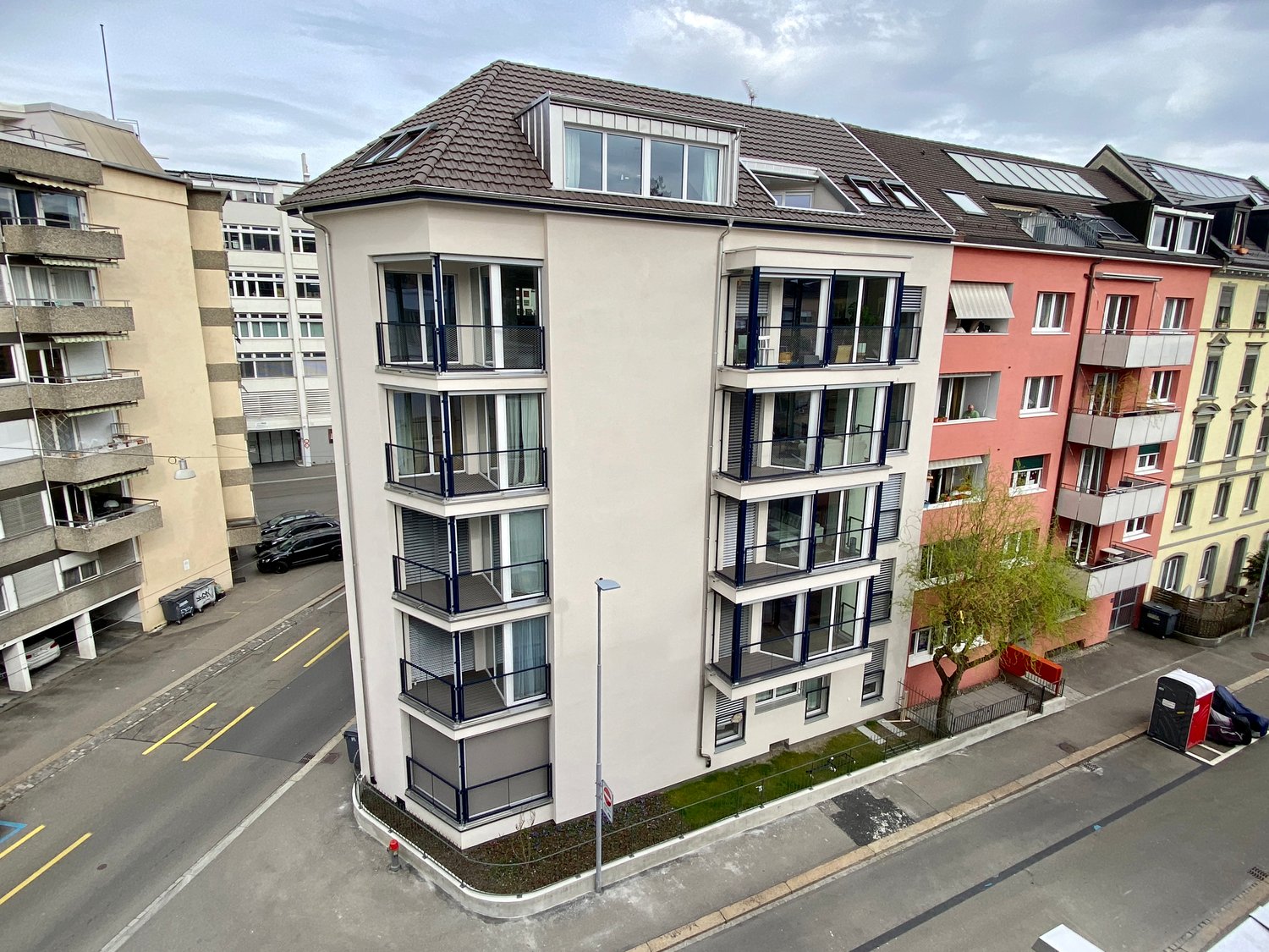 Apartment building, balconies on each floor, grey exterior, windows with white frames, street view